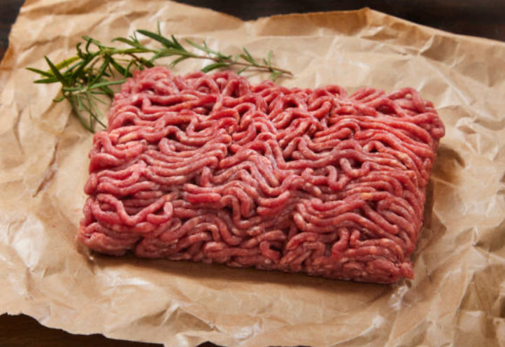 A rectangular portion of winterscattleranch Extra Lean Grass-Fed Ground Beef Bundles (available in 5–60 lb) sits on brown parchment paper, garnished with fresh rosemary.