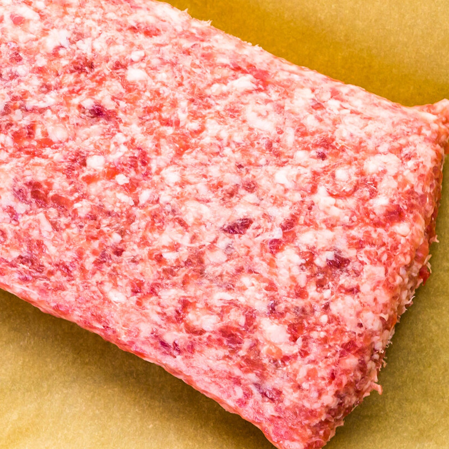 A close-up of Winters Cattle Ranch Ground Pork, a rectangular block with visible fat marbling, resting on brown parchment paper.