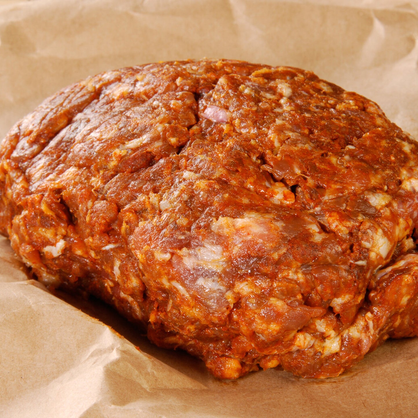 Winters Cattle Ranch Ground Pork & Sausage rests on brown parchment paper, its rich reddish hue revealing flavorful spices and the premium quality of heritage pork raised on a Colorado family farm.