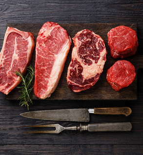 Five raw beef steaks of different cuts from Winters Cattle Ranch are arranged on a dark wooden board with rosemary—ideal for those interested in the 1/2 Beef Herd Share 6-month Subscription. A carving fork and knife rest below on the wooden surface.