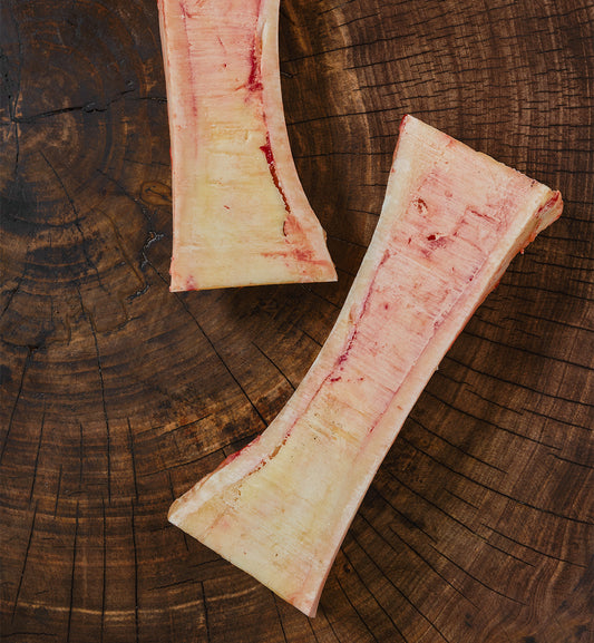 Two winterscattleranch Beef Bones - For Pets are displayed on a round, dark wooden surface with visible tree rings and textures.