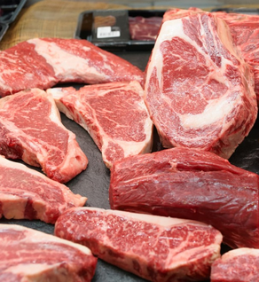 Various raw cuts from winterscattleranch’s Premium Organic Raised, Free-Range Grazing (Eighth of a Cow) Beef Bundle, including steaks and ribeye, are arranged on a dark surface with packaged meat in the background.