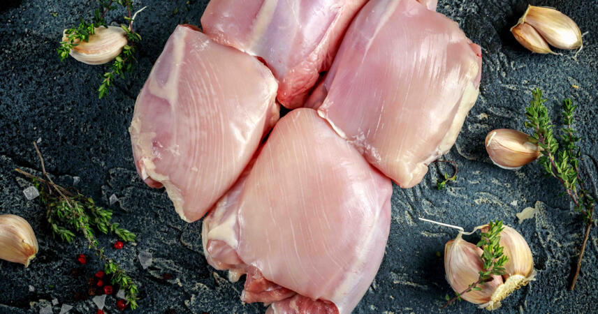 Five raw, skinless Chicken Organically Raised thighs from Winters Ranch, LLC arranged on a dark surface with thyme, garlic cloves, peppercorns, and coarse salt. Price is per pound.