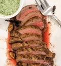 Winters Cattle Ranch Beef Tenderloin Roast deposits, sliced medium-rare, are served on a white plate with roasted garlic, green herb sauce, and a fork. Juices from this premium-grade beef enhance the presentation.