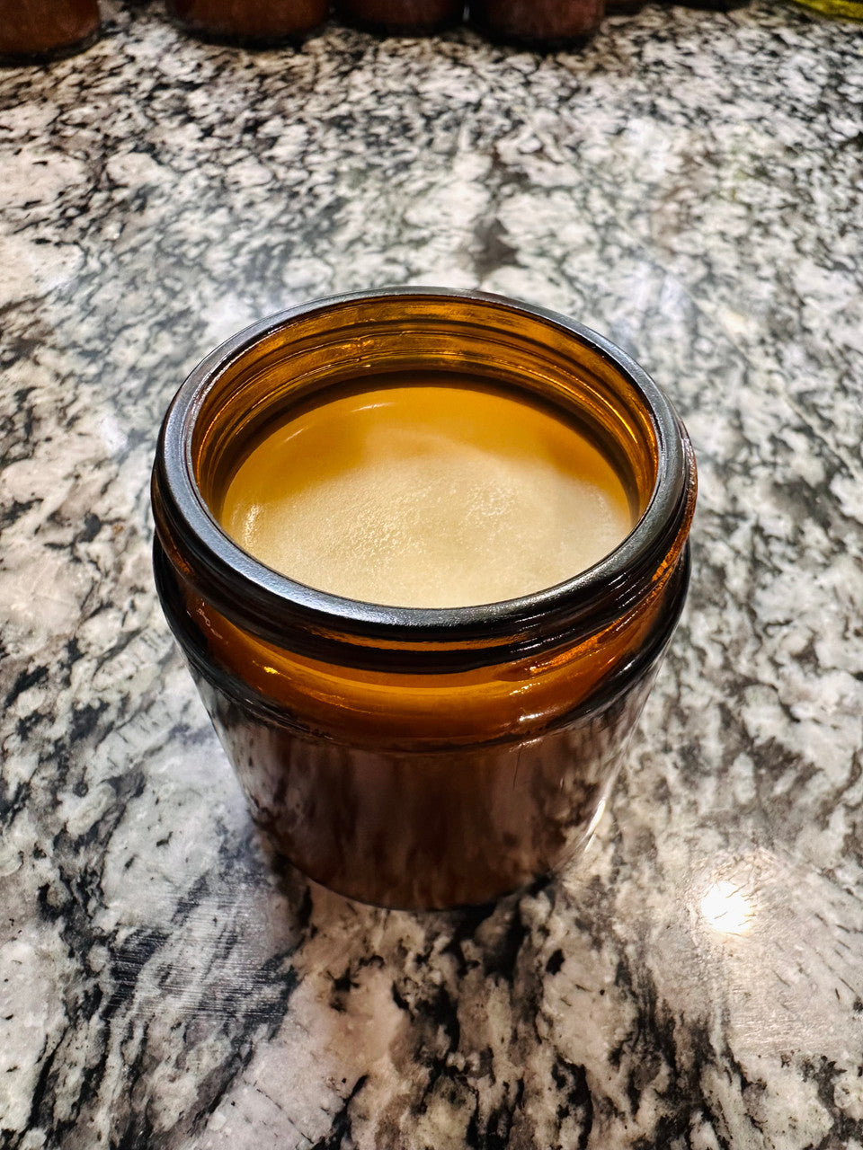 A jar of Winters Ranch, LLC Tallow sits open on a marbled countertop, displaying its smooth, light tan balm inside.