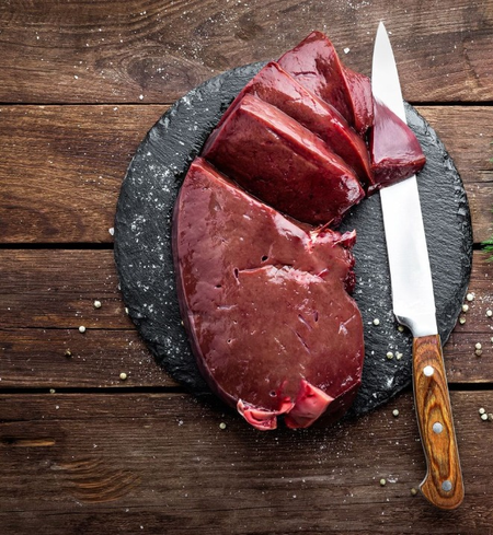 Premium Organic Raised, Free-Range Grazing (Beef Liver) by winterscattleranch sliced on a black slate plate with a kitchen knife, set on a wooden table sprinkled with salt and peppercorns.