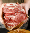 A person holds several raw, marbled cuts of red meat wrapped in brown butcher paper, preparing to cook or store them.
