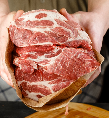 A person holds several raw, marbled cuts of red meat wrapped in brown butcher paper, preparing to cook or store them.