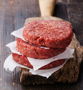Four Premium Organic Raised, Free-Range Hamburger Patties by winterscattleranch, each 1/3 lb, are stacked with parchment paper between them on a rustic cutting board against a dark wooden background.